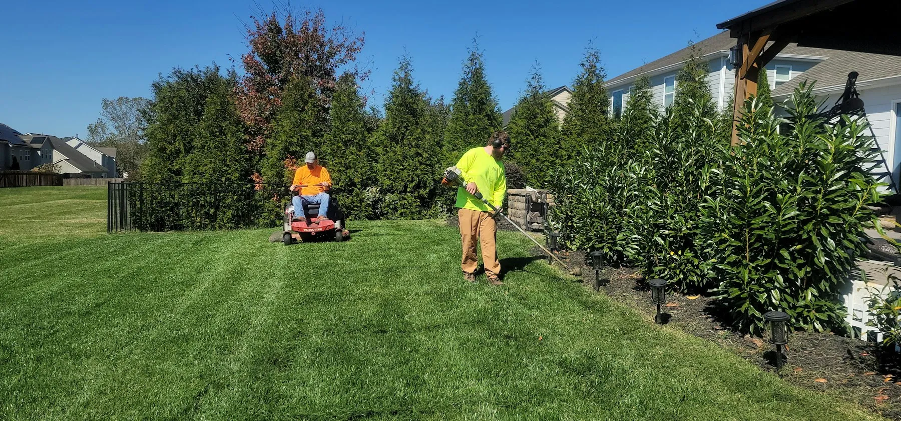 Crew mowing a lawn in straight stripes along a hedge line