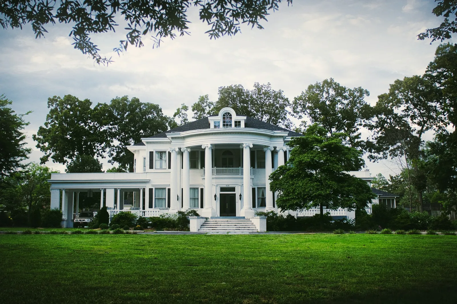 Large white home with a manicured lawn and mature oaks