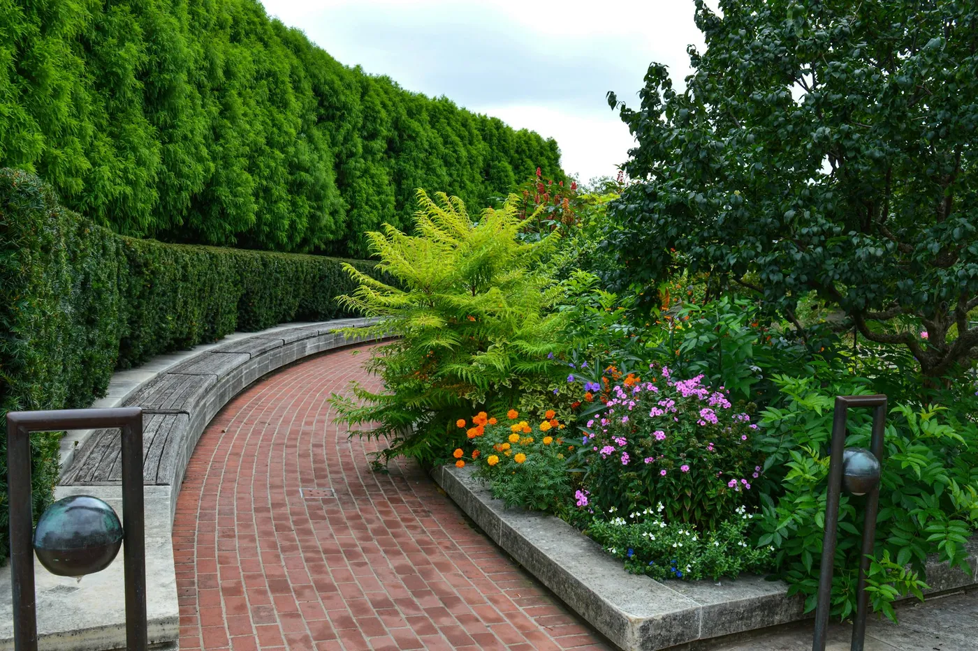 Brick garden path lined with flowering beds and a tall hedge